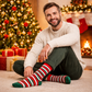 Man sitting on the floor wearing festive striped socks with a Christmas tree and presents in the background.
