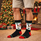 Person wearing festive socks with a Christmas tree and stockings in the background