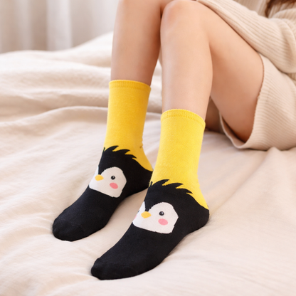Yellow and black penguin crew socks worn by a person sitting on a beige surface.
