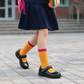 Person wearing a navy skirt, black shoes, and yellow socks with polka dots on a paved walkway.