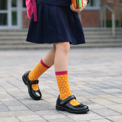 Person wearing a navy skirt, black shoes, and yellow socks with polka dots on a paved walkway.