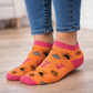 Orange Ankle Halloween socks with insect patterns and pink toes worn with blue jeans on a wooden floor.