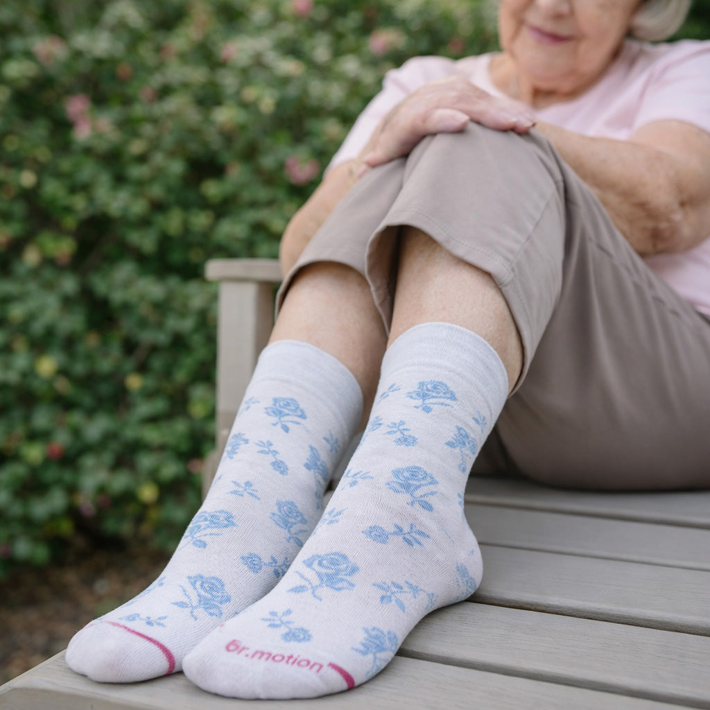 Person wearing light gray socks with blue floral patterns, sitting outdoors.