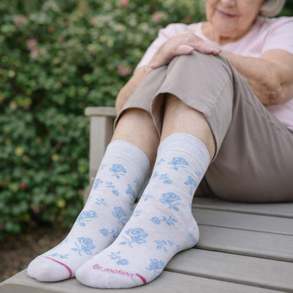 Person wearing light gray socks with blue floral patterns, sitting outdoors.