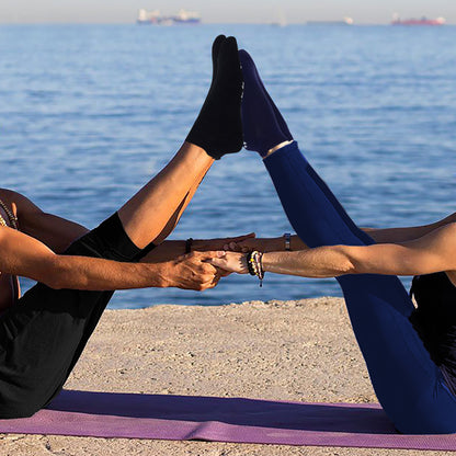 Two people wearing yoga socks doing yoga by the water with a clear sky.